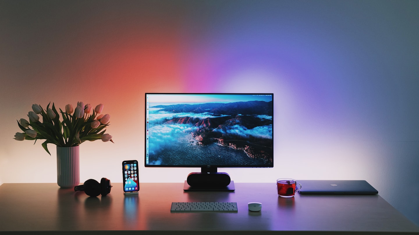 A modern office desk with a computer displaying a cloudscape and white tulips.