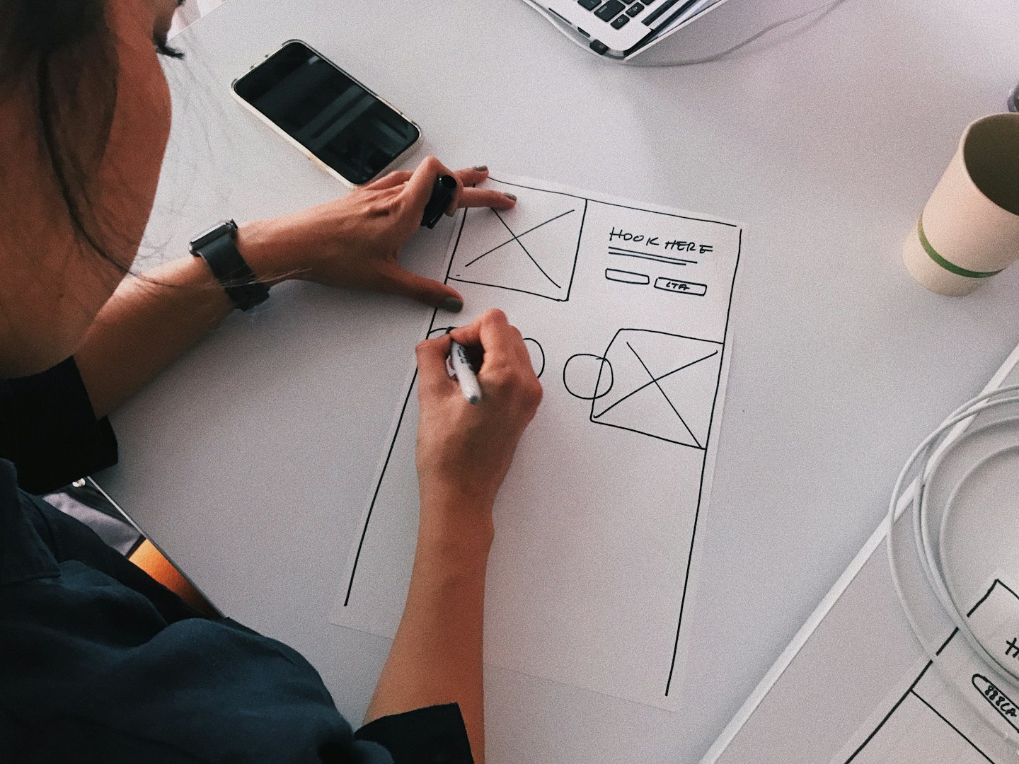 Designer sketching website wireframe with labels on desk.