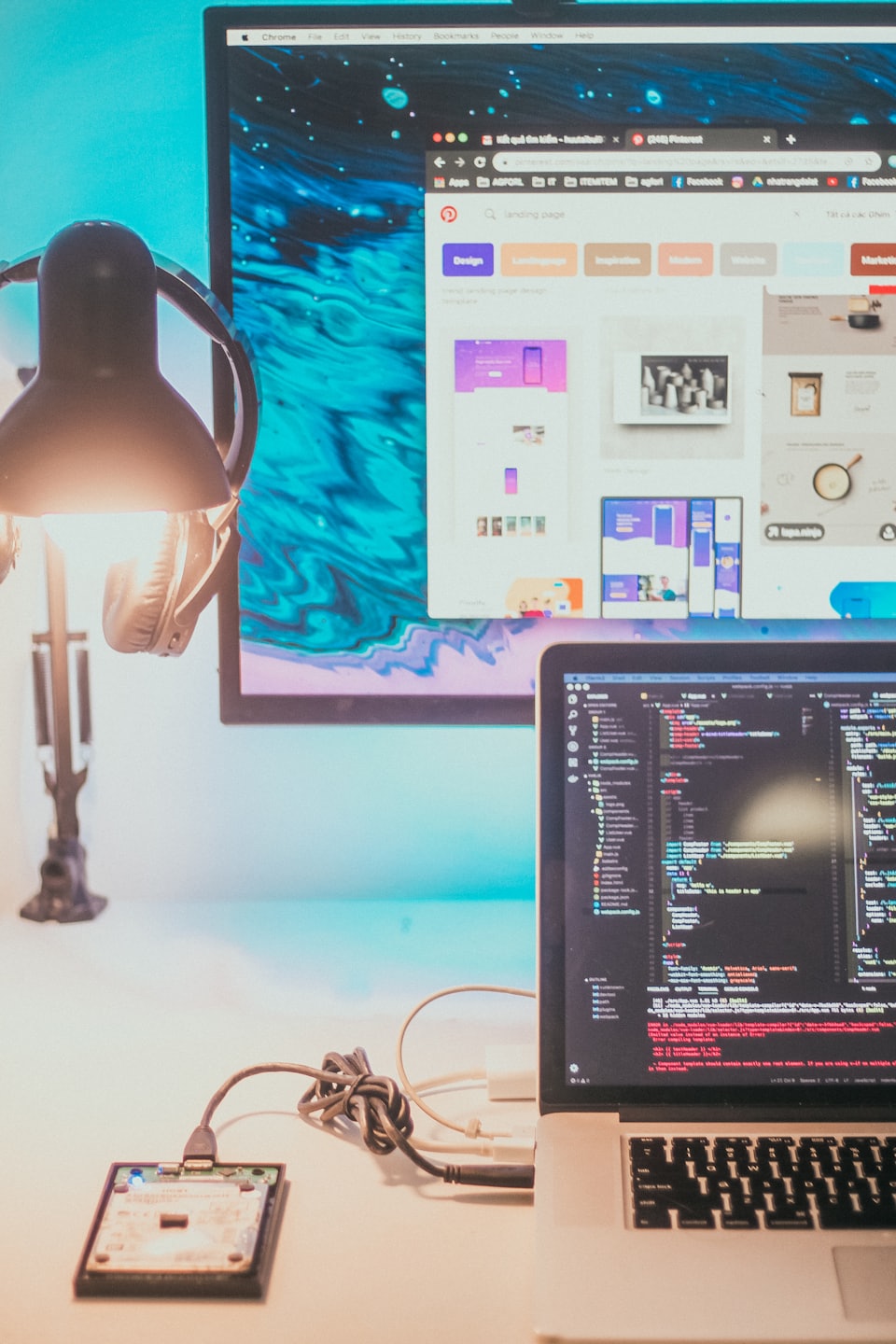 Laptop and monitor displaying programming code on a cluttered desk.