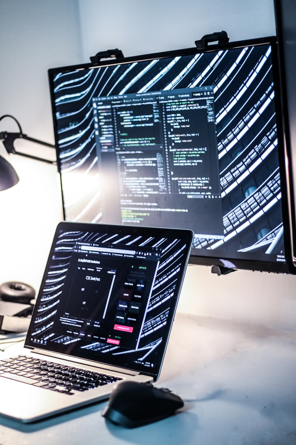 Laptop and monitor displaying code in a modern office.